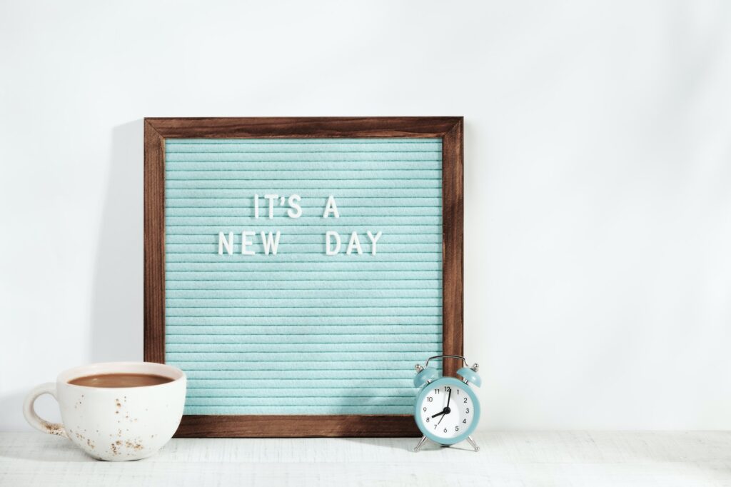 It's a new day. Alarm clock, cup of coffee and letter board with a motivating phrase stand on table.